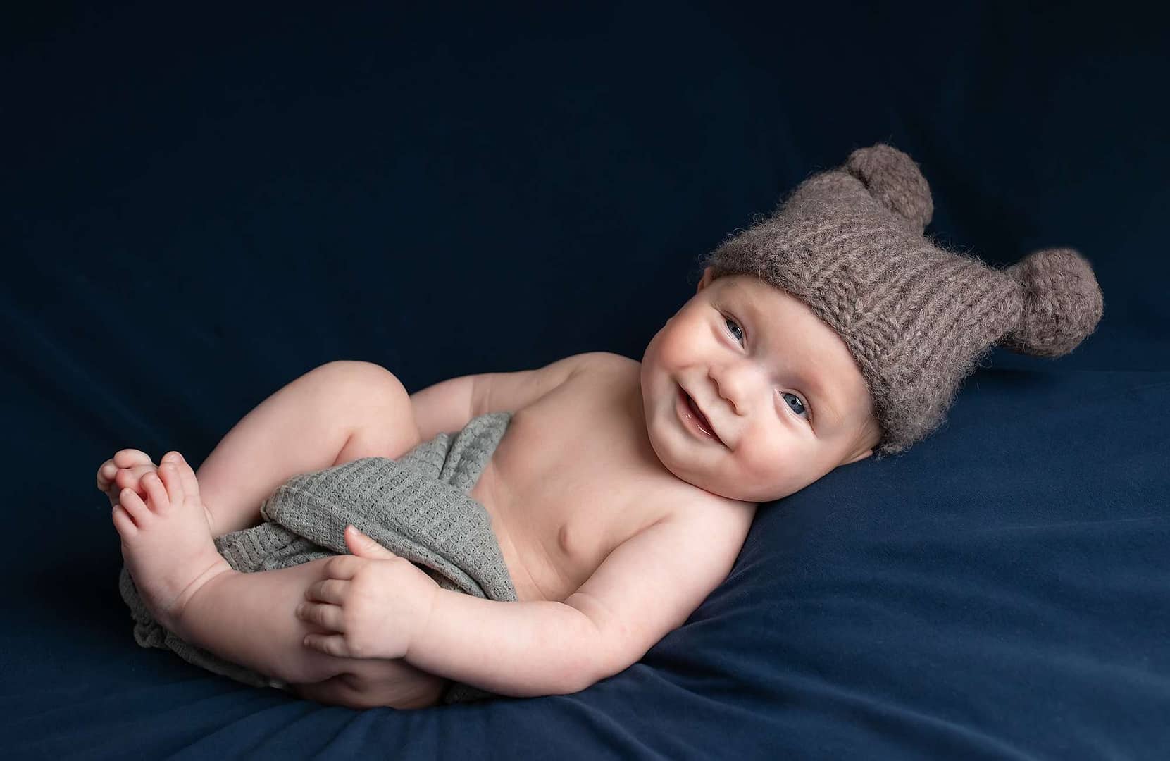 smiling baby boy in pom pom hat during photoshoot for older baby in haywards heath