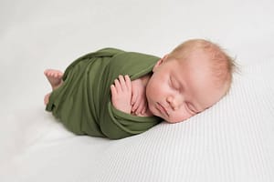 burgess hill photographer shows image of swaddled sleeping baby in green wrap on white background
