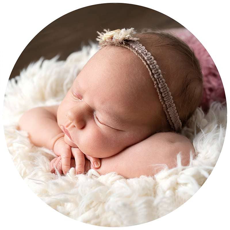 newborn baby girl lying with head on arms wearing headband during west sussex newborn photoshoot